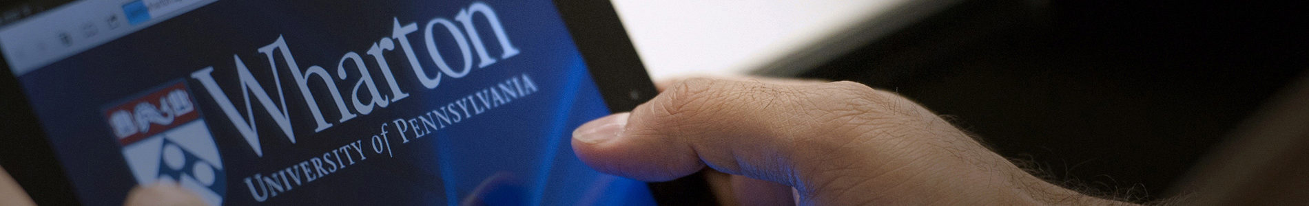 A person holding a tablet displaying the Wharton School logo, University of Pennsylvania.